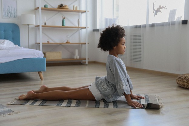 Young girl doing a yoga pose on mat in her bedroom.